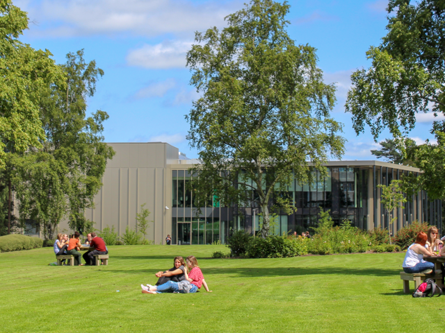 People sitting on benches and on a lawn of grass on the Heriot-Watt University Edinburgh campus