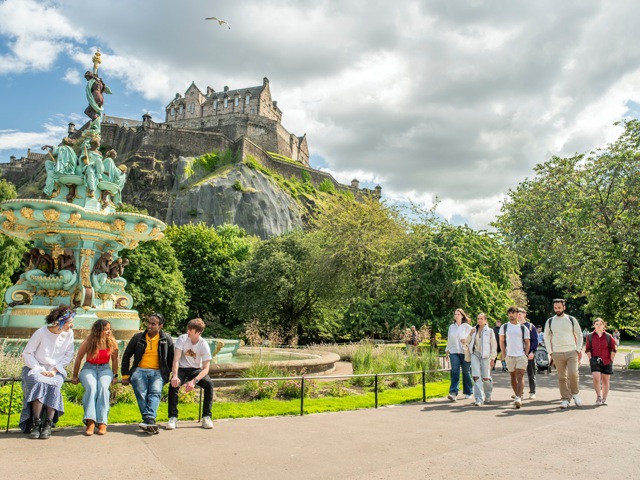 Students walking through Princes Street Gardens in Edinburgh on a sunny day with the castle in background.