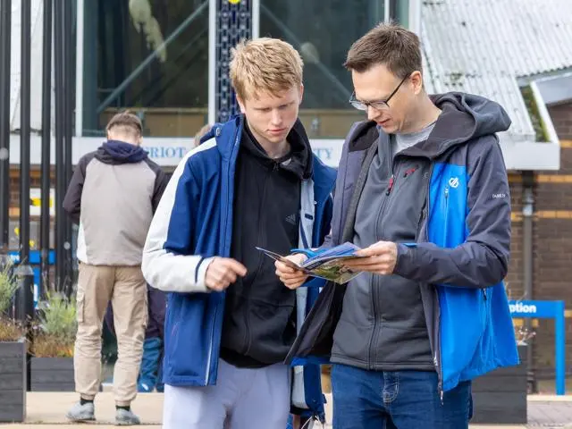 Two people looking at a brochure in front of the main entrance to the Edinburgh Campus
