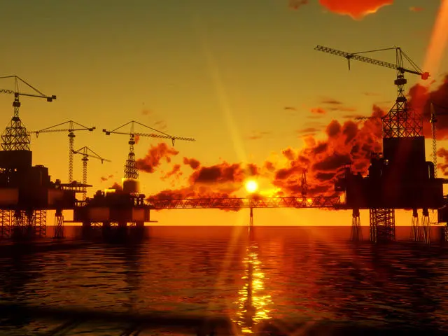 Silhouetted oil rigs at sea during sunset with cranes