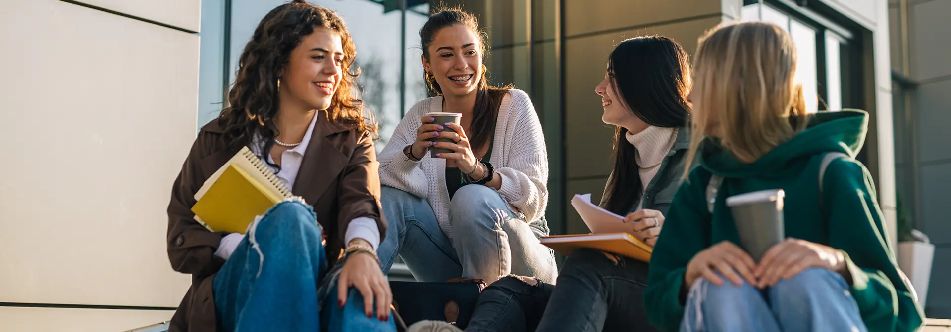 Four students sitting outside together drinking coffee.