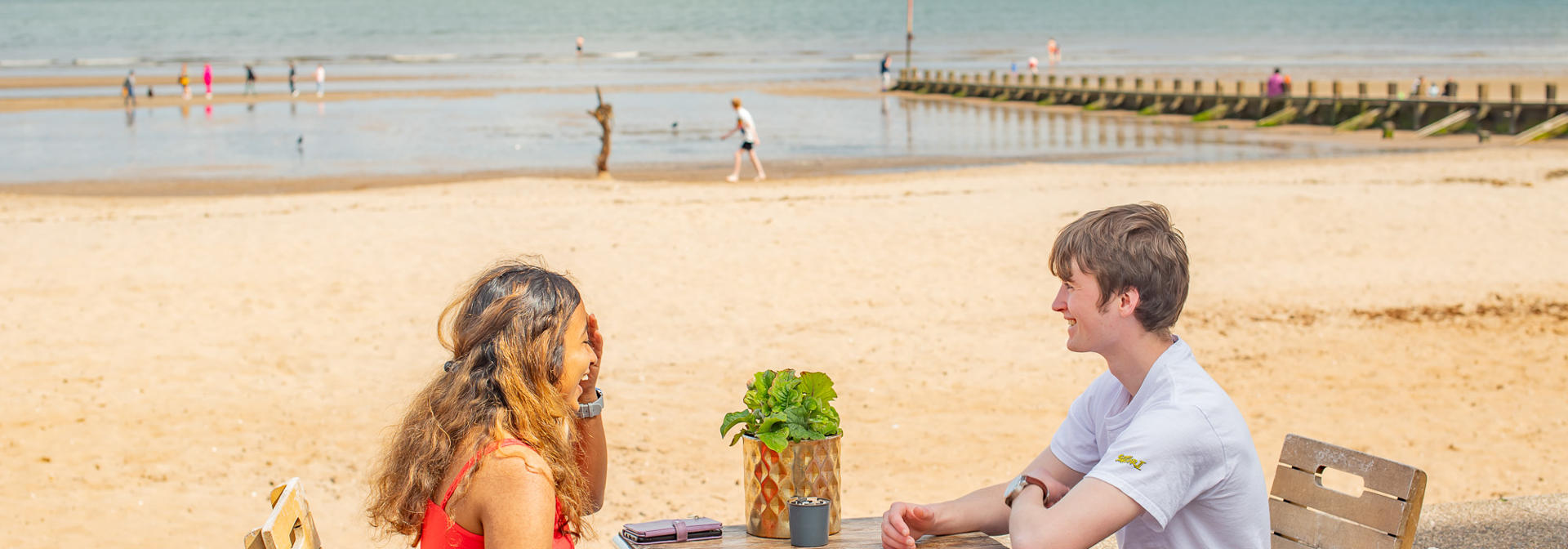 Two individuals talking while sat at a table beside the beach.