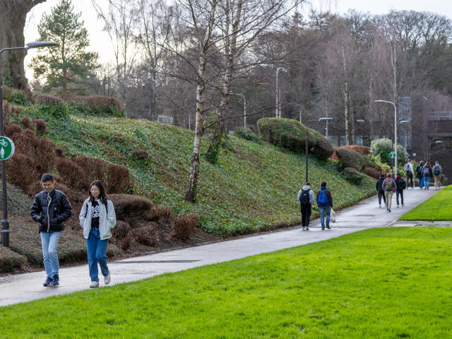 Two individuals walking along a path outside with grass and nature either side.