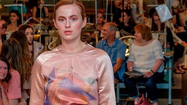 female model walking runway, wearing a pink long sleeve satin top with an abstract planet print