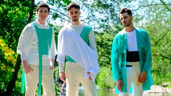 three male models standing at the edge of a river, all wearing tan trousers with green different green white and tan layered tops 