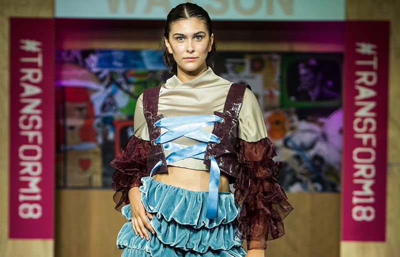 woman walking runway, wearing a beige satin top with brown ruched long sleeves, a brown corset tied in front with a light blue ribbon and ruched loose light blue velvet trousers
