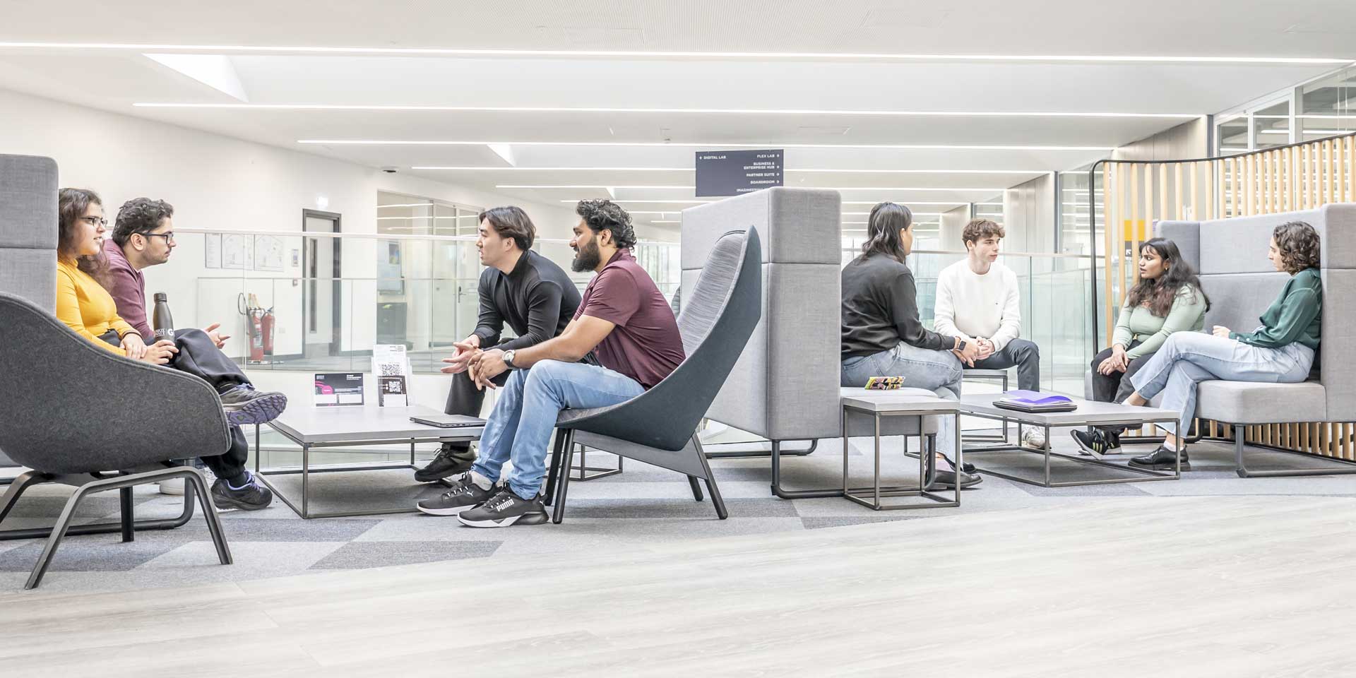 Two groups of seated students in the GRID building break out area.