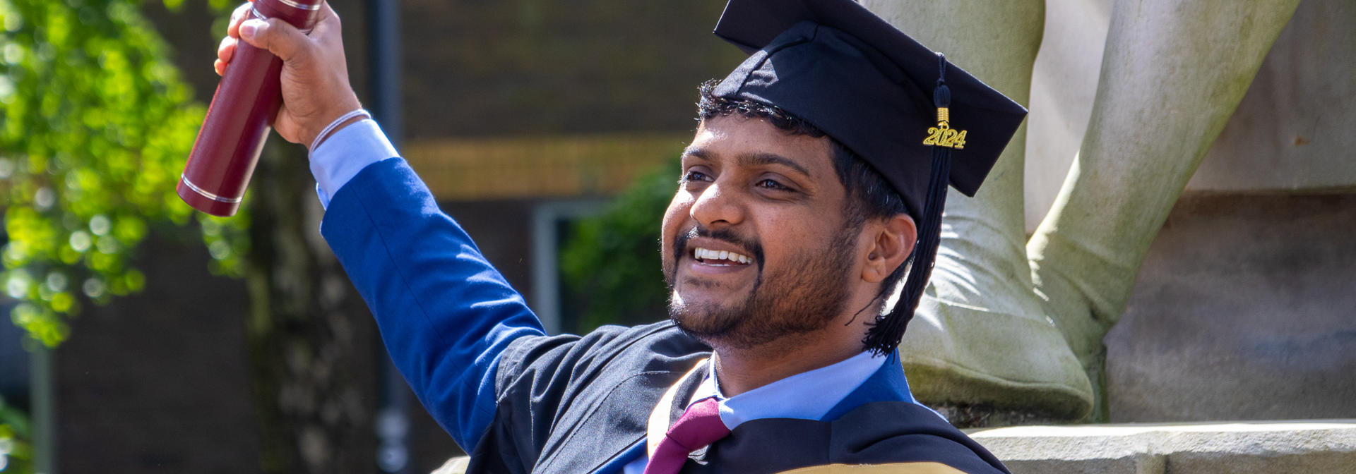 Graduate smiling and waving his degree certificate scroll