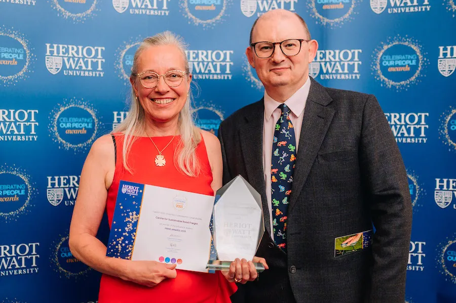 Teo individuals smiling as they receive an award and certificate. 