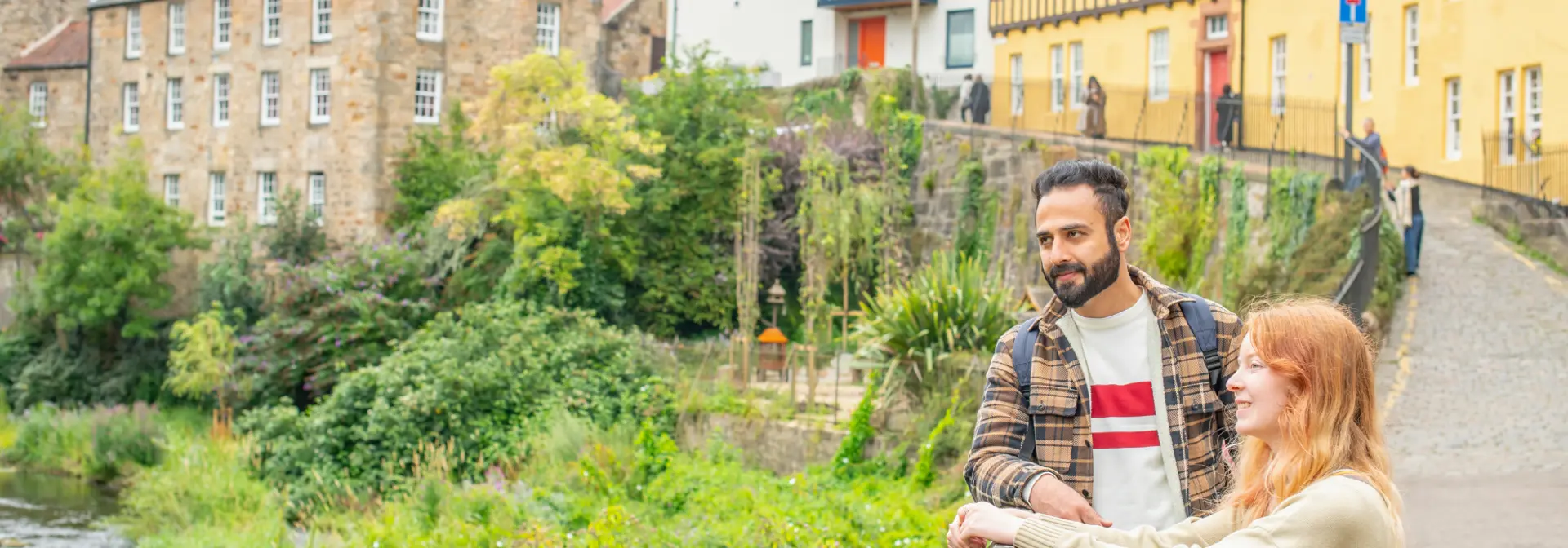 Two students standing by a fence overlooking the Water of Leith in the historic Dean Village, Edinburgh city.