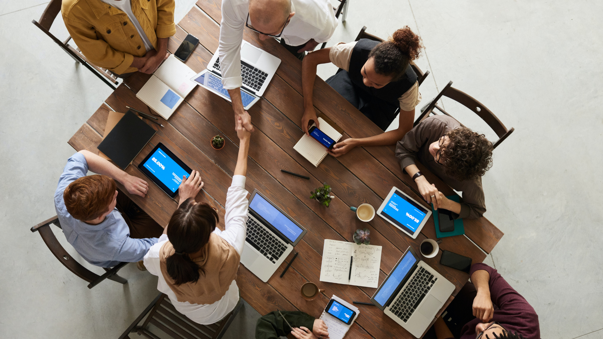 A birds-eye view of two people shaking hands over a table at a meeting.