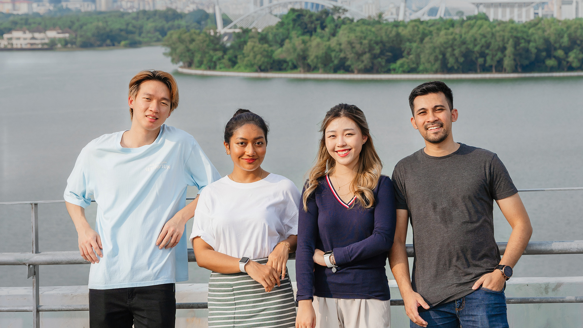 Four students standing together by a fence with a lake behind them. 