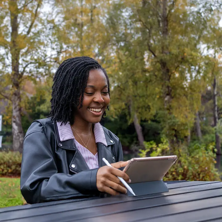 Naomi, a current student, working on an ipad outside at a bench on the Edinburgh campus.
