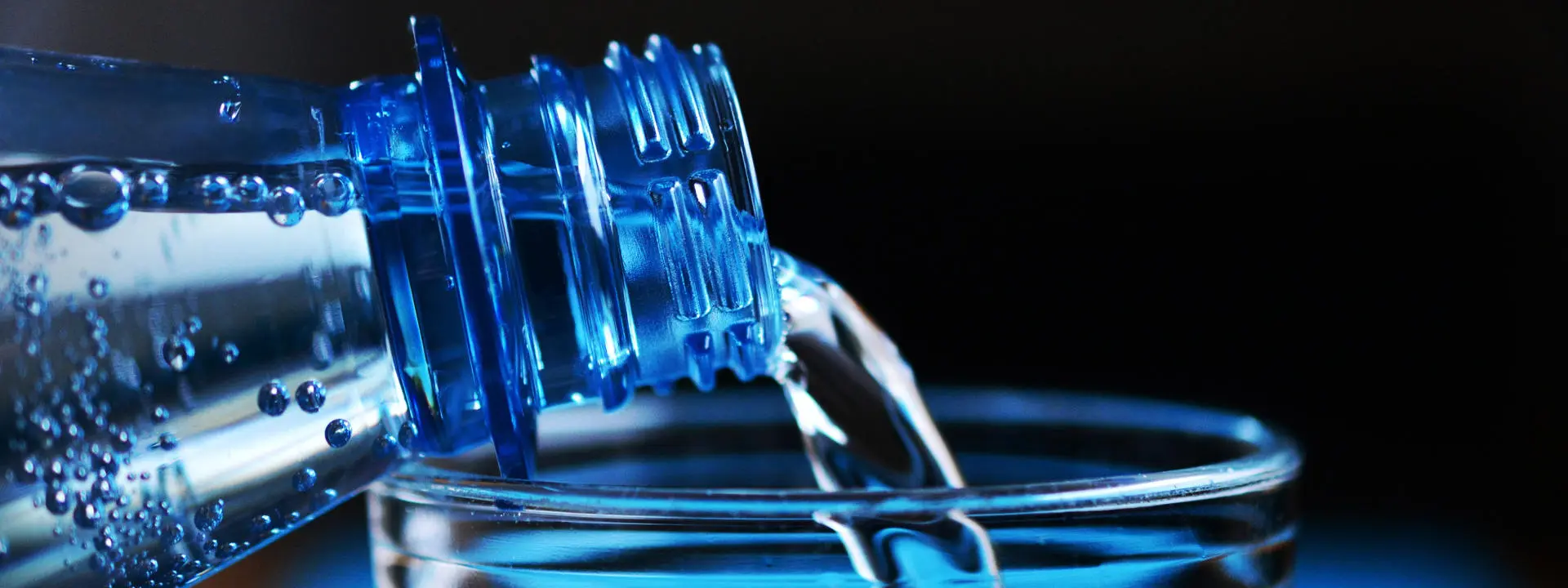 Close-up of sparkling water being poured from a blue plastic bottle into a glass.