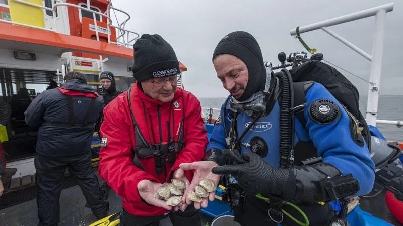Hamish Torrie and Dr Bill Sanderson, on a boat, holding oysters