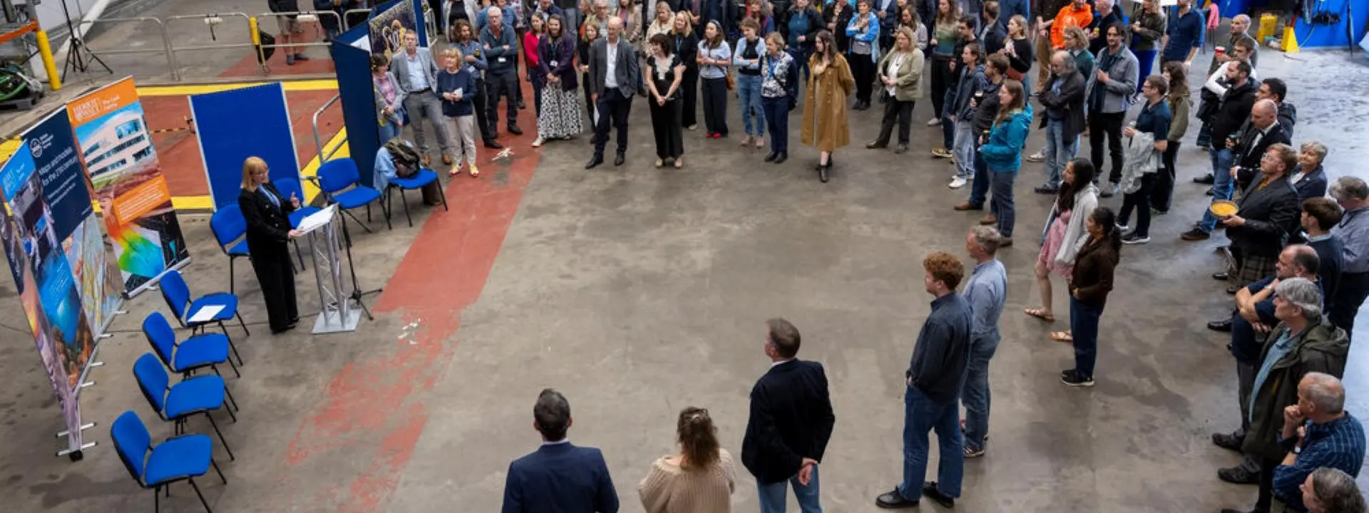 A group of people gathers round as a speech is given.