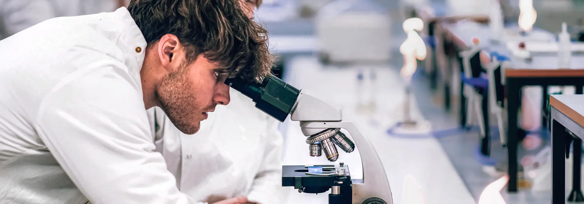 Biology student looking through microscope while his lab partner watches