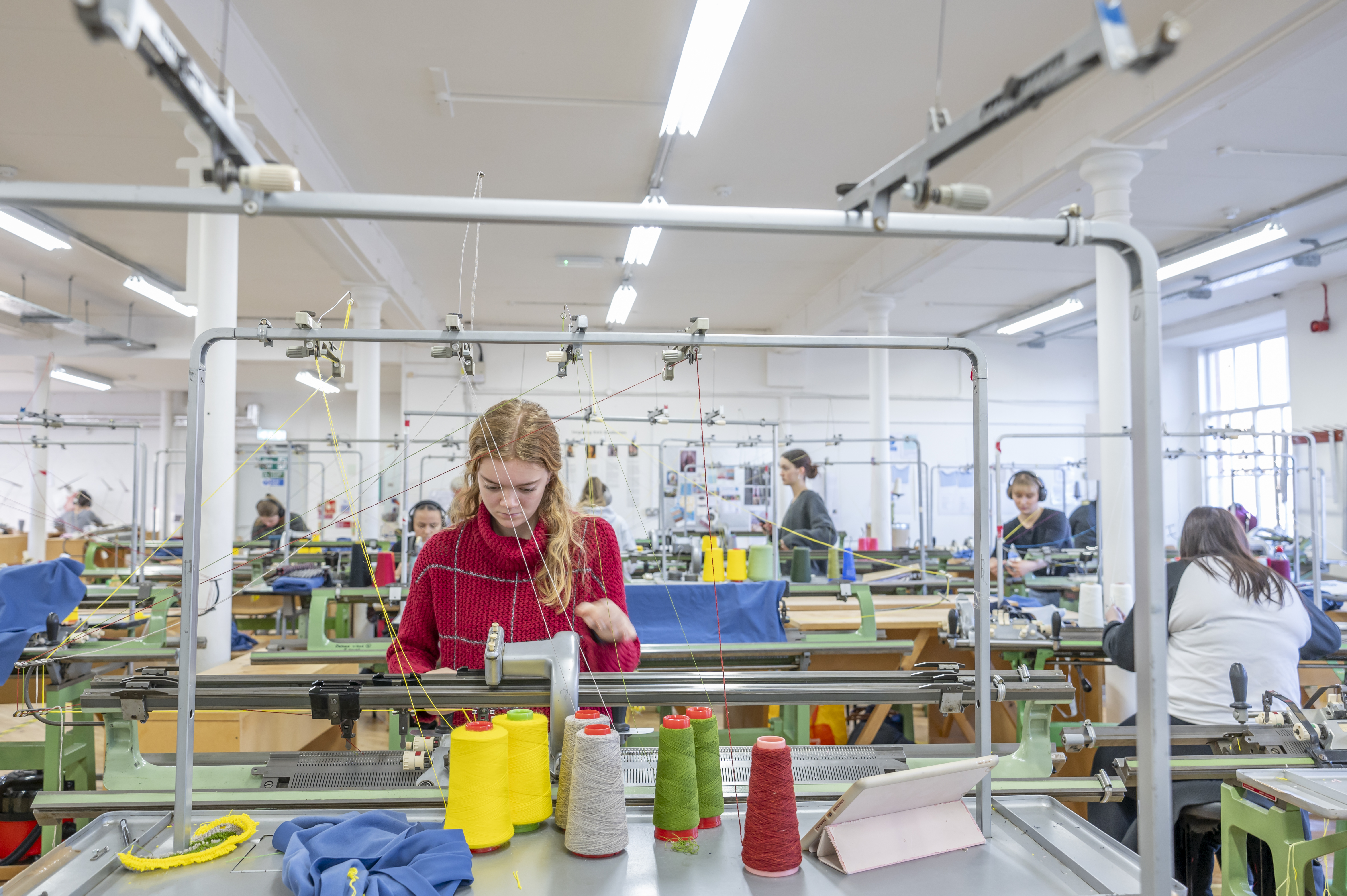 Student working on a knit machine in busy studio.