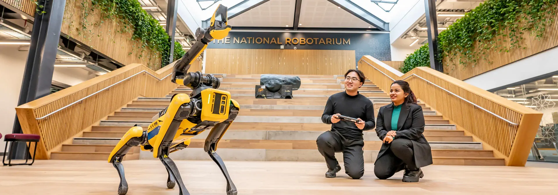 Two students operate a robot dog using a handheld console in the National Robotarium