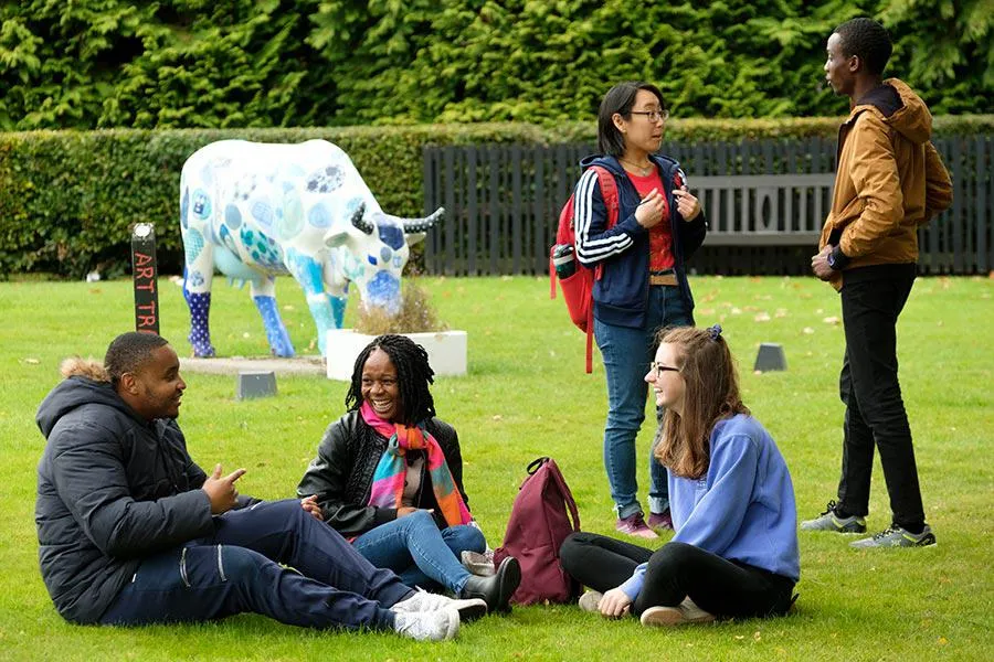 The 'Watt a Clever Cow' staute was designed by staff and students in the School of Textiles and Design Students sitting on grass beside a statue of a cow